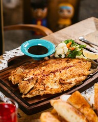 Grilled flounder fish with vegetables being served on wooden plate