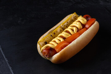 classic hot dog with meat sausage, fried cheese, fresh tomatoes and cheese sauce on dark stone background with copy space