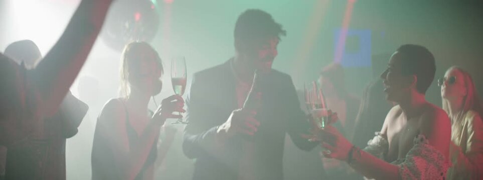 Slow-motion shot of a young man in the dance club pouring beer into glasses for everyone and cheering with each other