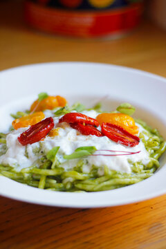 Close-up of Italian trofia pasta with pesto, burrata cheese and cherry tomatoes served on a white plate. Italian (Ligurian) cuisine, selective focus, copy space