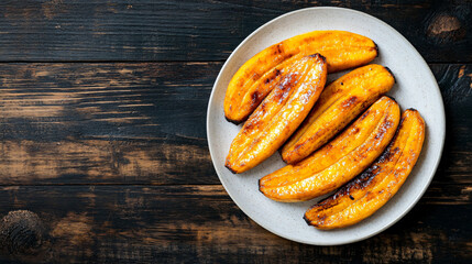 Sweet fried plantains on a dark wooden table, topped with brown sugar and suitable for vegetarians and vegans. Rustic backdrop with room for text