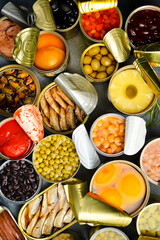 A large assortment of canned preserves food in tin open cans. On a gray stone background. Food banner. Top view.