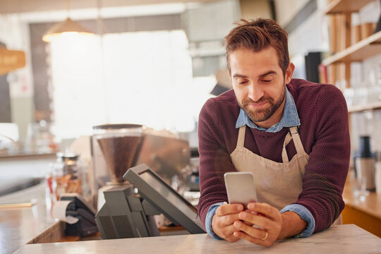 Businessman, barista and cafe with phone for online order, service or social media at coffee shop. Happy man, waiter or business owner with smile on mobile smartphone for review at indoor restaurant