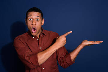 Photo portrait of nice young man amazed point hold empty space wear trendy brown outfit isolated on dark blue color background