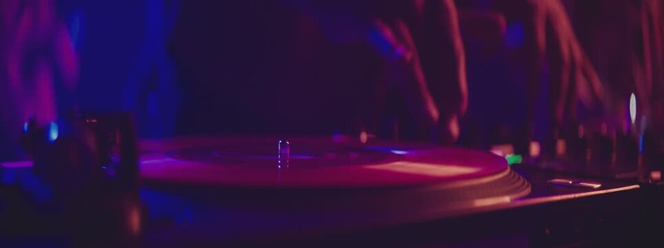 Hip hop dj scratching vinyl record on turntables against a background of dancing people in night club. Professional disc jockey plays music