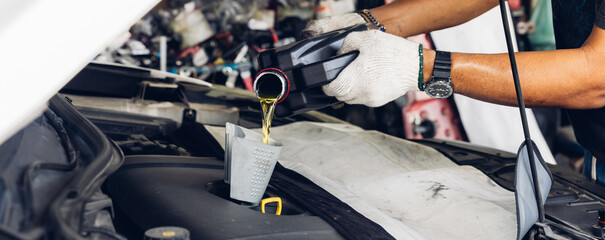 Car mechanic replacing and pouring fresh oil into engine at maintenance repair service station,