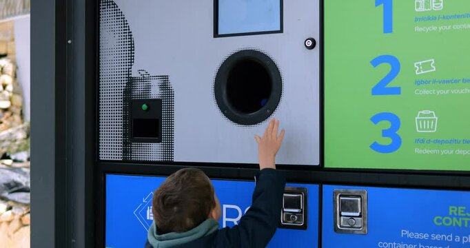 Little boy inserts plastic bottle into reverse vending machine on city street. Toddler child learns to sorts garbage for environment conservation
