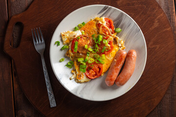 Eggs with tomatoes and fried sausage in a gray plate on a round wooden stand nearby fork