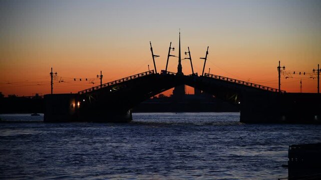 Side view of opening bascule bridge with blurred Saints Peter and Paul Cathedral at sunrise in Saint Petersburg city, Russia. Black silhouettes of buildings. Real time video. Travel in Russia theme.
