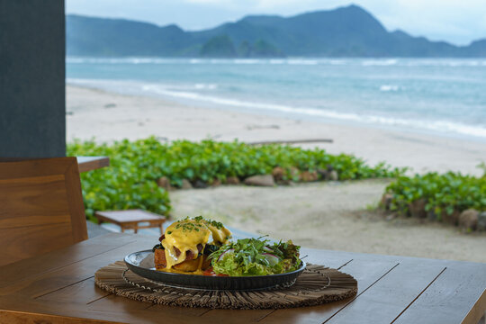 Close-up of a plate of Eggs florentine on a table with a beach background, Indonesia