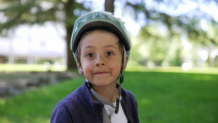 Portrait of young boy wearing bike helmet, smiling, sitting in a park, sunny day, safety gear, enjoying outdoors, cheerful expression, child in nature, active lifestyle, happy and carefree moment