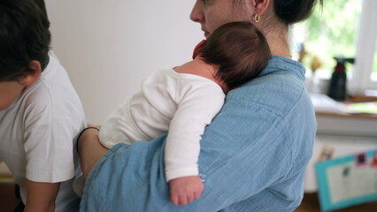 Fototapeta premium Mother holding a baby and comforting another child while multitasking. the essence of parenthood, balancing love and care for her children in a serene home setting