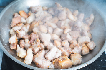 Pork, cut into pieces, is fried in a metal pan.