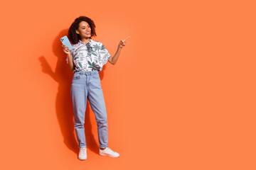 Photo of brown haired curly girl in summer shirt holding mobile phone pointing finger target advert isolated on orange color background