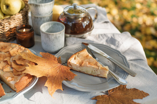 Close-up of a slice of apple pie and tea with a basket of apples on an autumnal garden table