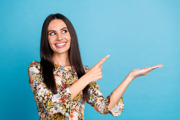 Photo of adorable lovely girl wear flower print dress pointing holding arm empty space isolated blue color background