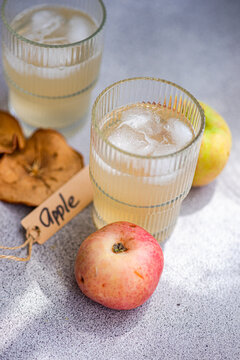 Close-up of two glasses of fresh apple juice on a table mat with fresh apples, dried apple slices and a tag with the word apple