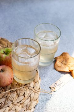 Close-up of two glasses of fresh apple juice on a table mat with fresh apples, dried apple slices and a tag with the word apple