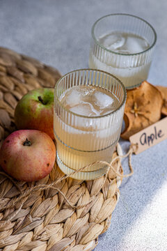Close-up of two glasses of fresh apple juice on a table mat with fresh apples, dried apple slices and a tag with the word apple