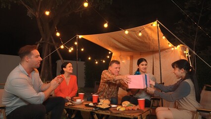 Family together celebrate anniversary in garden. Senior give gift to granddaughter. Outdoor camping activity to relax with relatives, spend time with multigeneration cross generation gap. Divergence.