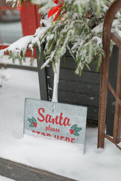 Close-up of a Santa Please Stop Here sign by a Christmas tree outside a house on a snowy winter day, Belarus