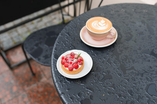 Cappuccino and a fresh raspberry tart on a wet table in an outdoor cafe