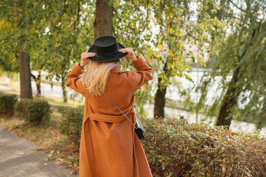 Rear view of a woman in a wool coat standing in a park adjusting her hat on an autumn day, Belarus