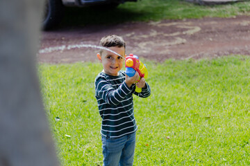 Little child playing with his toy in the park in a sunny day. Having fun with a water gun on summer vacation. Caucasian and beautiful kid. 