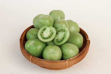 Close up of fresh green tomatoes in a woven bamboo container on an isolated background.