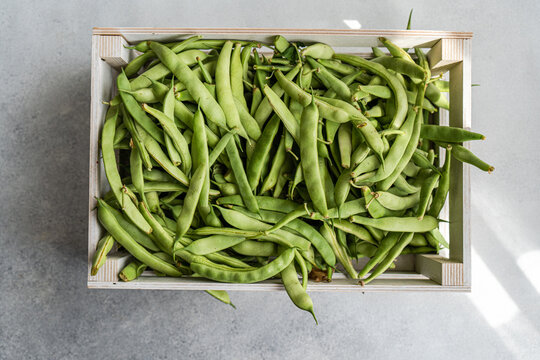 Overhead view of fresh organic runner beans in a wooden crate on a table