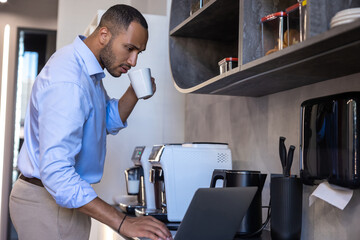 Obraz premium African American man wearing blue shirt working on laptop in kitchen