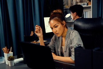 Serious face of thinking businesswoman focusing computer to report data analysis social media online project job with coworker working at back side at over late night time at modern office. Infobahn.