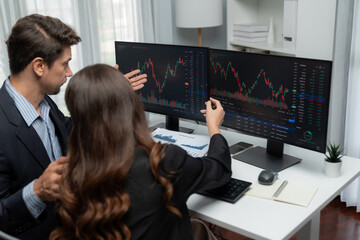 Two business traders discussing on dynamic stock market in currency rate investment trading on two pc screens with compare real time graph on risk or profit point of data at modern office. Postulate.