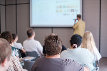 Group of people attending educational seminar focused on speaker presenting digital content on...