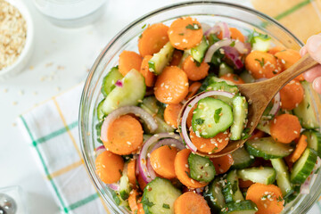 Hand holding wooden spoon with fresh carrot cucumber salad with sesame seeds. Top view. Eating...