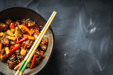 Pork in sweet and sour sauce with pineapple, capsicum, ginger in a bowl on a gray background. Copyspace. Close-up.