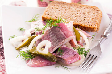 Traditional matie herring salad with onion rings and gherkins served as close-up with a rustic wholemeal bread on a design plate