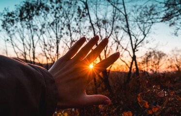 The rays of the sun break through the fingers of a woman's hand. A feeling of coziness, calm, happiness, freedom and relaxation. An escape from the hustle and bustle.