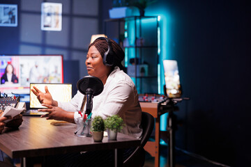 Female celebrity is seen answering interviewer questions in home studio, utilizing smartphone on tripod to record encounter. Black woman filming content for online audience, sharing exciting stories.