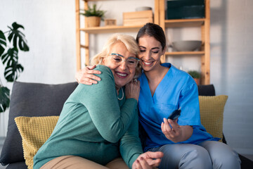 Obraz premium A smiling female nurse in scrubs assists a joyful elderly woman with a glucose test at her home, ensuring compassionate in-home medical support.