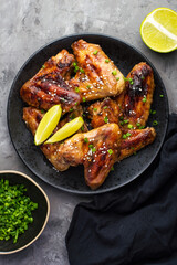 Japanese dish chicken wings with teriyaki sauce sprinkled with green onions and sesame seeds on a dark background.