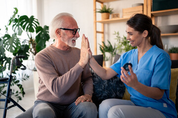 A smiling nurse in blue scrubs gives a high-five to an elderly patient as she conducts a glucose...