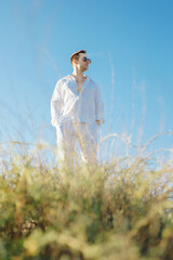 Elegant man in white pants and shirt posing at the nature