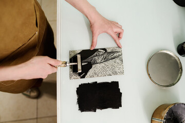 Top view of hands of young unrecognizable female designer or worker of printing house applying ink...