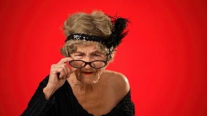 Funny view of unhappy displeased frustrated elderly woman saying NO wearing wig, glasses and no teeth isolated on red background