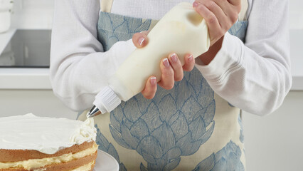 Closeup of a person using a piping bag to decorate cake.