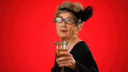 Fun smiling elderly woman 80s years old walks into frame drink wine, smiles and walks off frame, isolated on red background studio portrait .