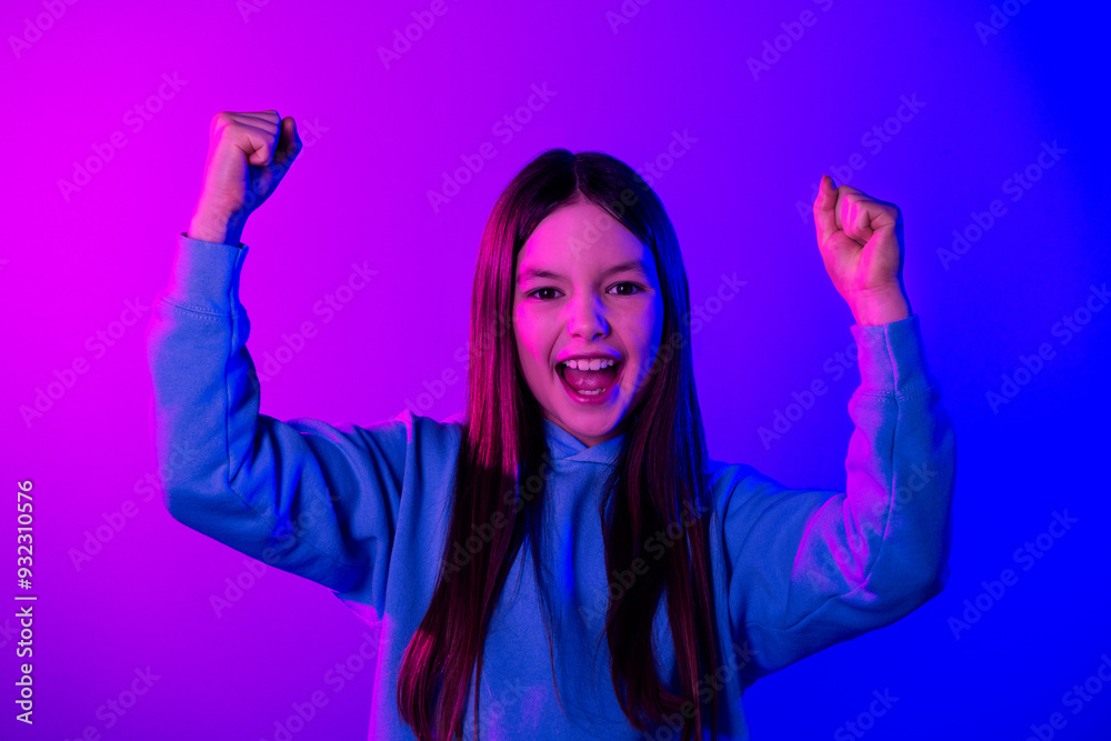 Wall mural photo of adorable lucky small girl wear hoodie rising fists empty space isolated magenta blue color 