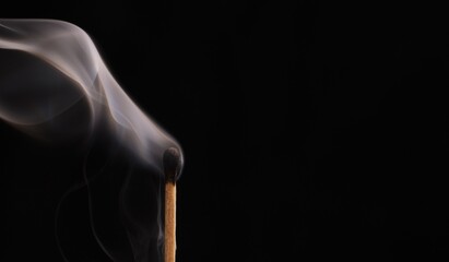 Burnt match with trailing smoke after being blown out on a black background