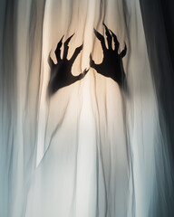 Dark clawed hands behind a white curtain forming a terrifying silhouette ideal for Halloween.